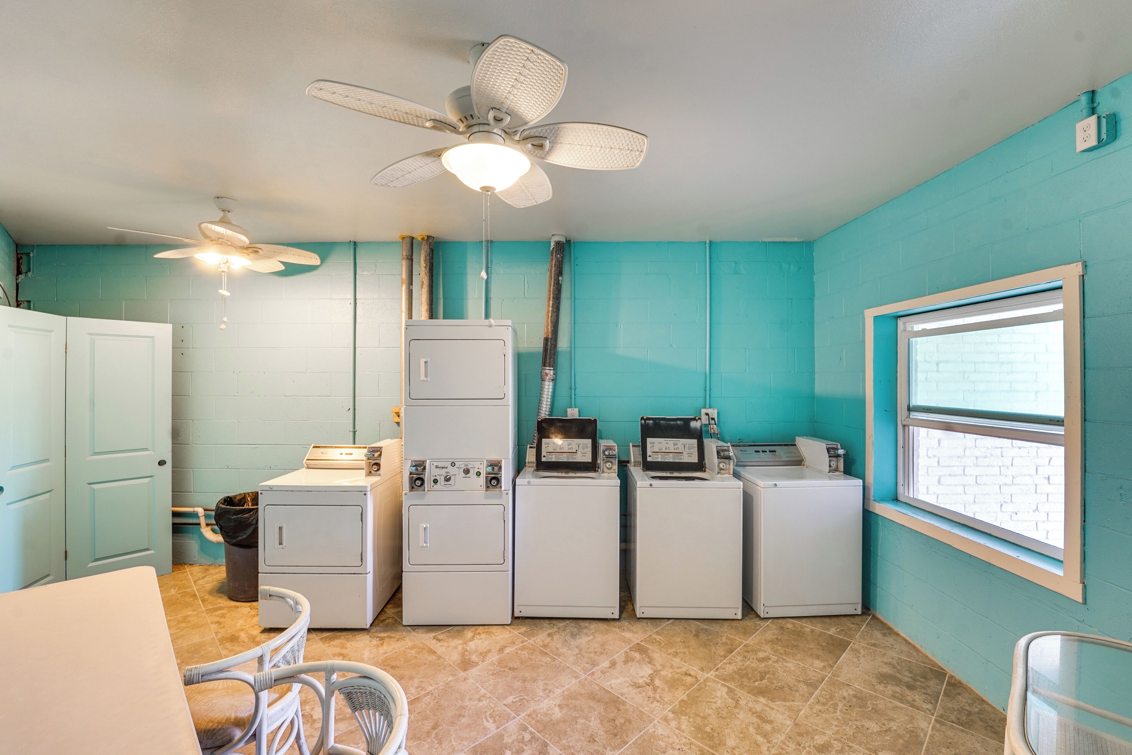 A laundry room with a ceiling fan, a window, and a row of washing machines.