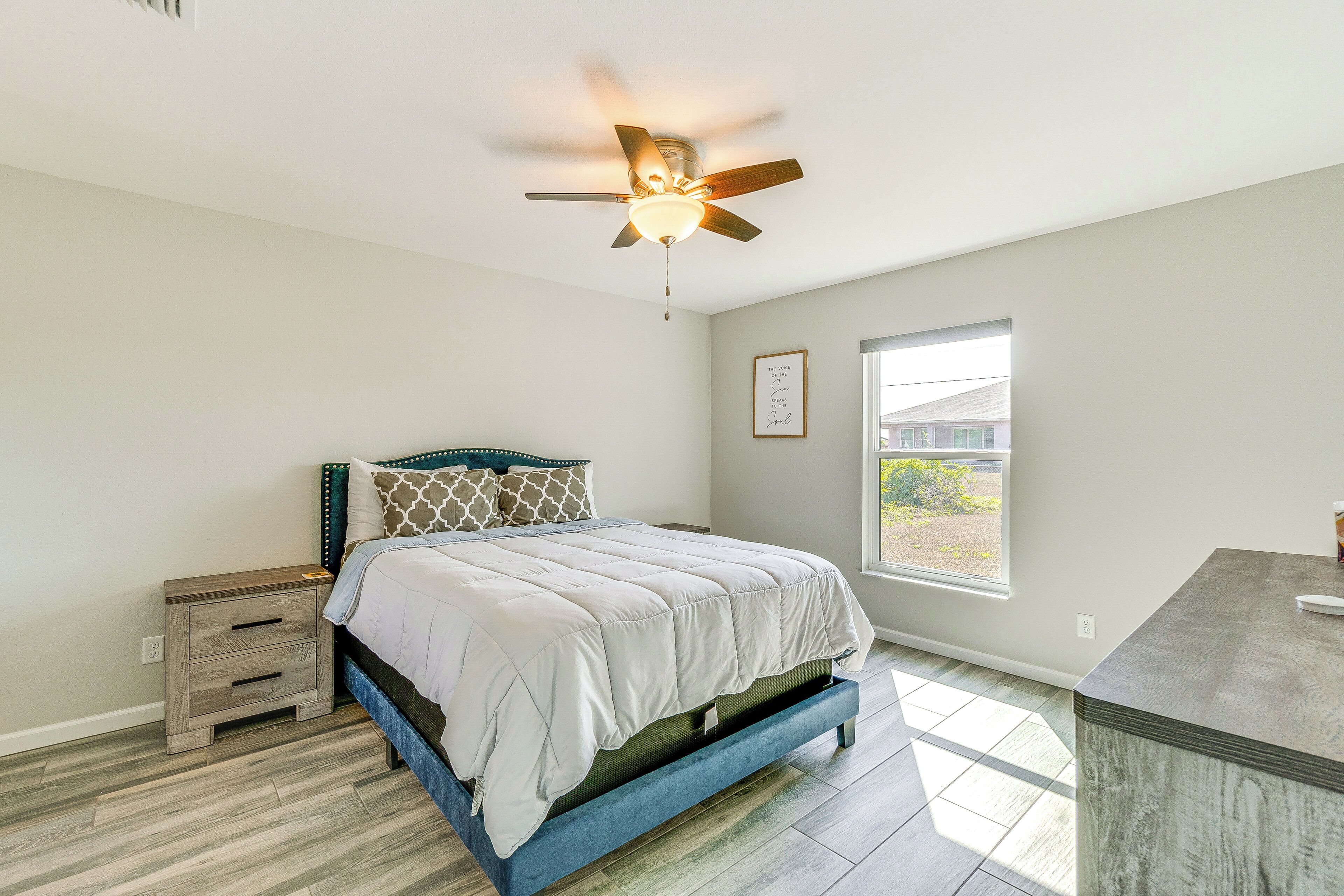 A bedroom with a bed, a nightstand, a ceiling fan, a window, and a view of the outside.
