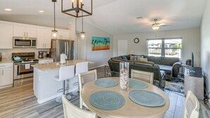 A modern kitchen with white cabinets, stainless steel appliances, and a dining area with a round table and blue placemats.