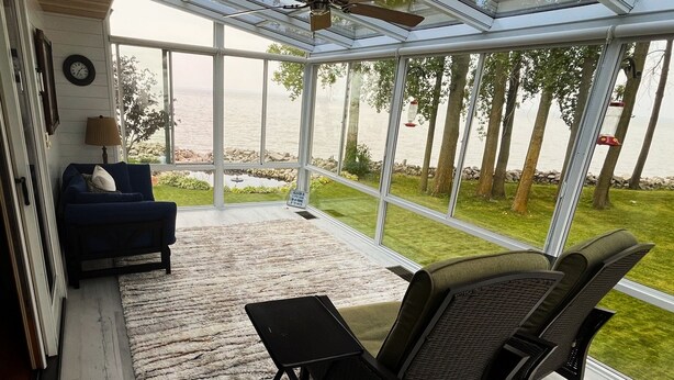 A covered patio with a view of a lake, a blue sofa, and a table.