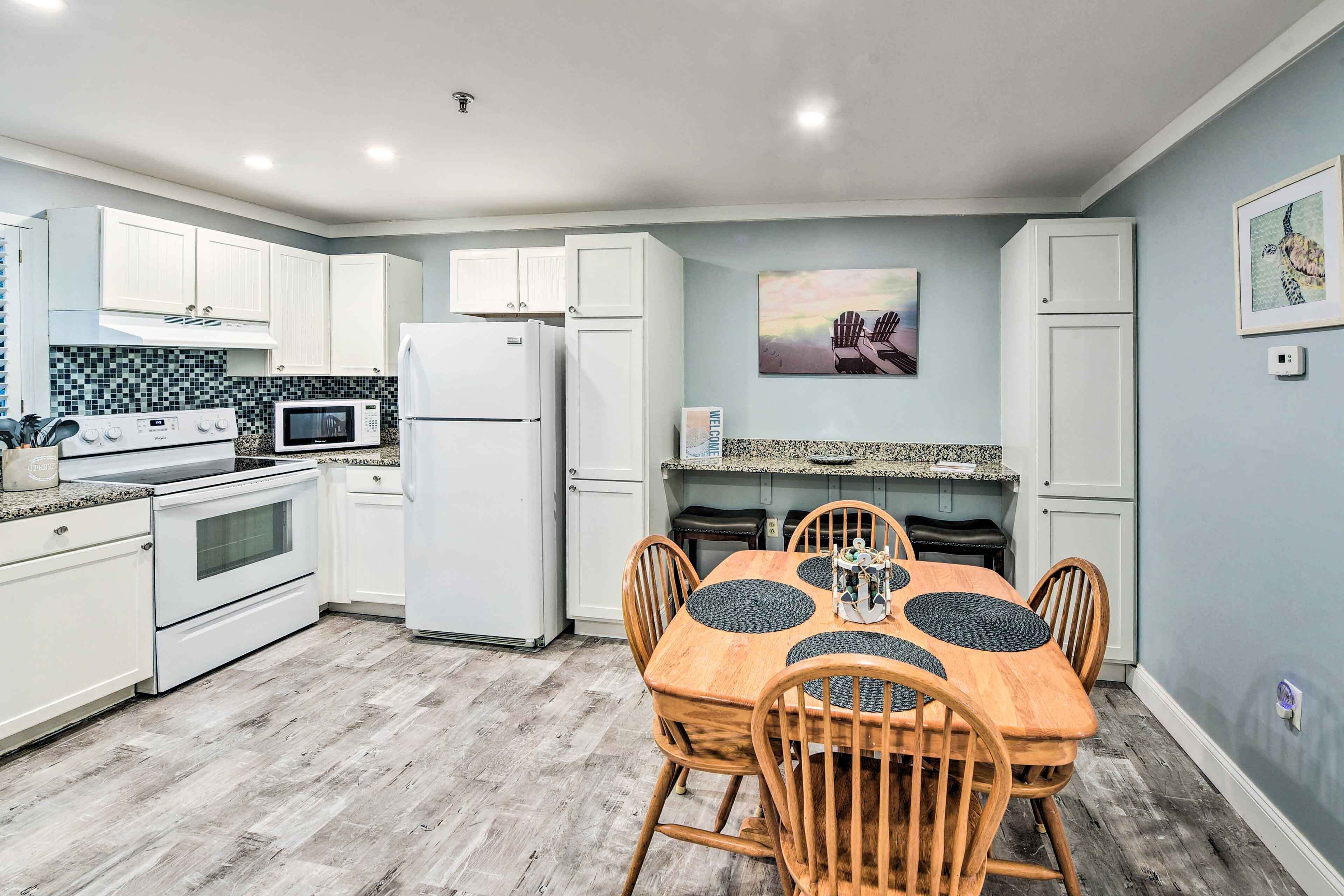Una cocina moderna con armarios blancos, microondas, refrigerador y una mesa de comedor con sillas.