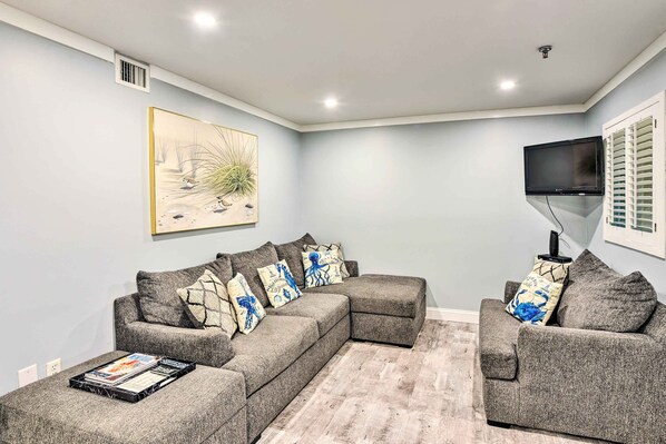 A modern living room with a sectional sofa, a flat-screen TV, and a large abstract painting on the wall. - Walk to Ocean: Condo w/ Community Perks on HHI (Hilton Head Island)