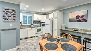 A modern kitchen with white cabinets, a granite countertop, and a dining area with a wooden table and chairs. - Walk to Ocean: Condo w/ Community Perks on HHI (Hilton Head Island)