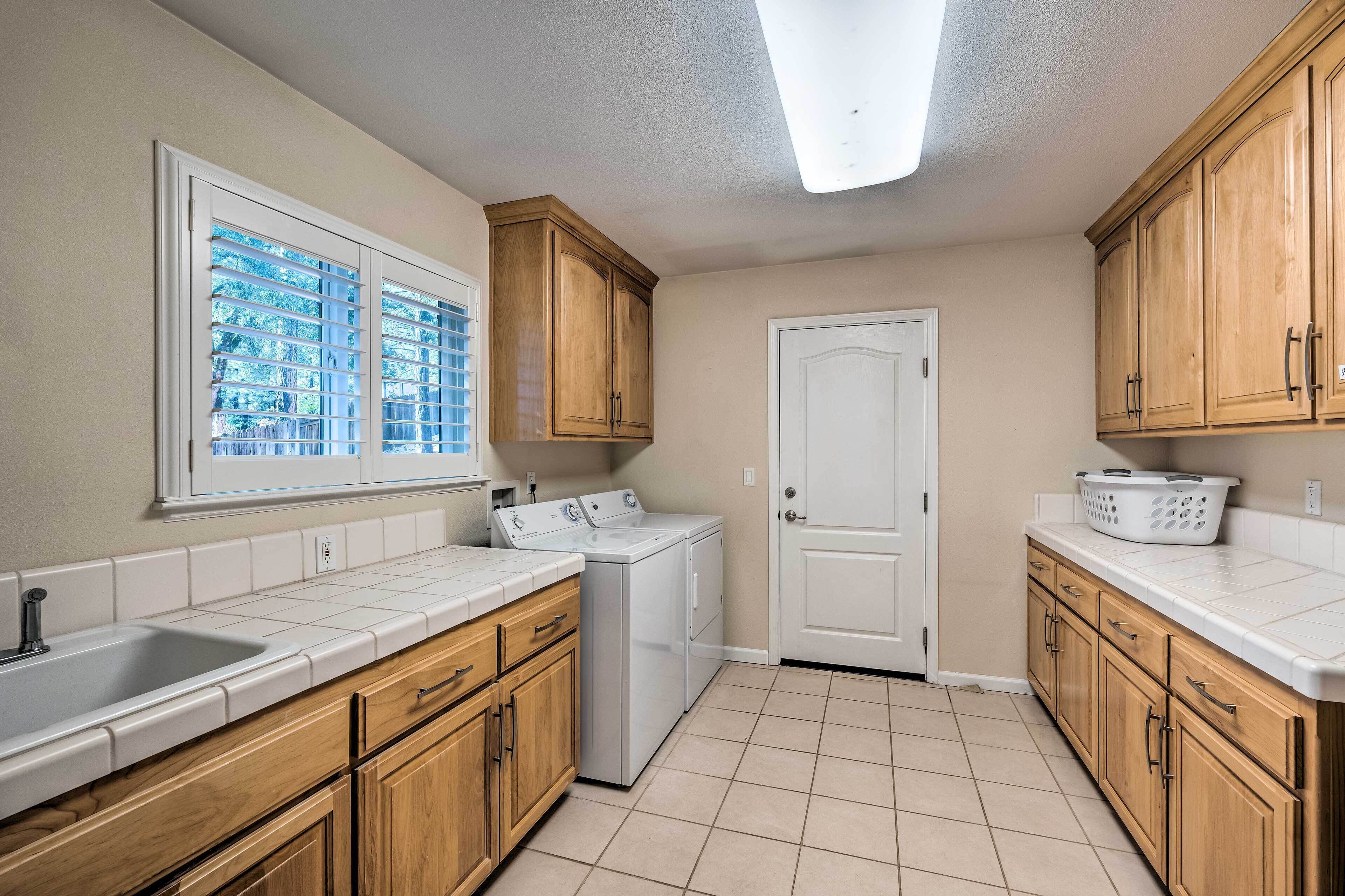 A kitchen with wooden cabinets, a built-in washer and dryer, a window with blinds, and a white door.