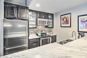 Uma cozinha moderna com armários escuros, eletrodomésticos de aço inoxidável, painel de azulejos e bancadas de mármore.