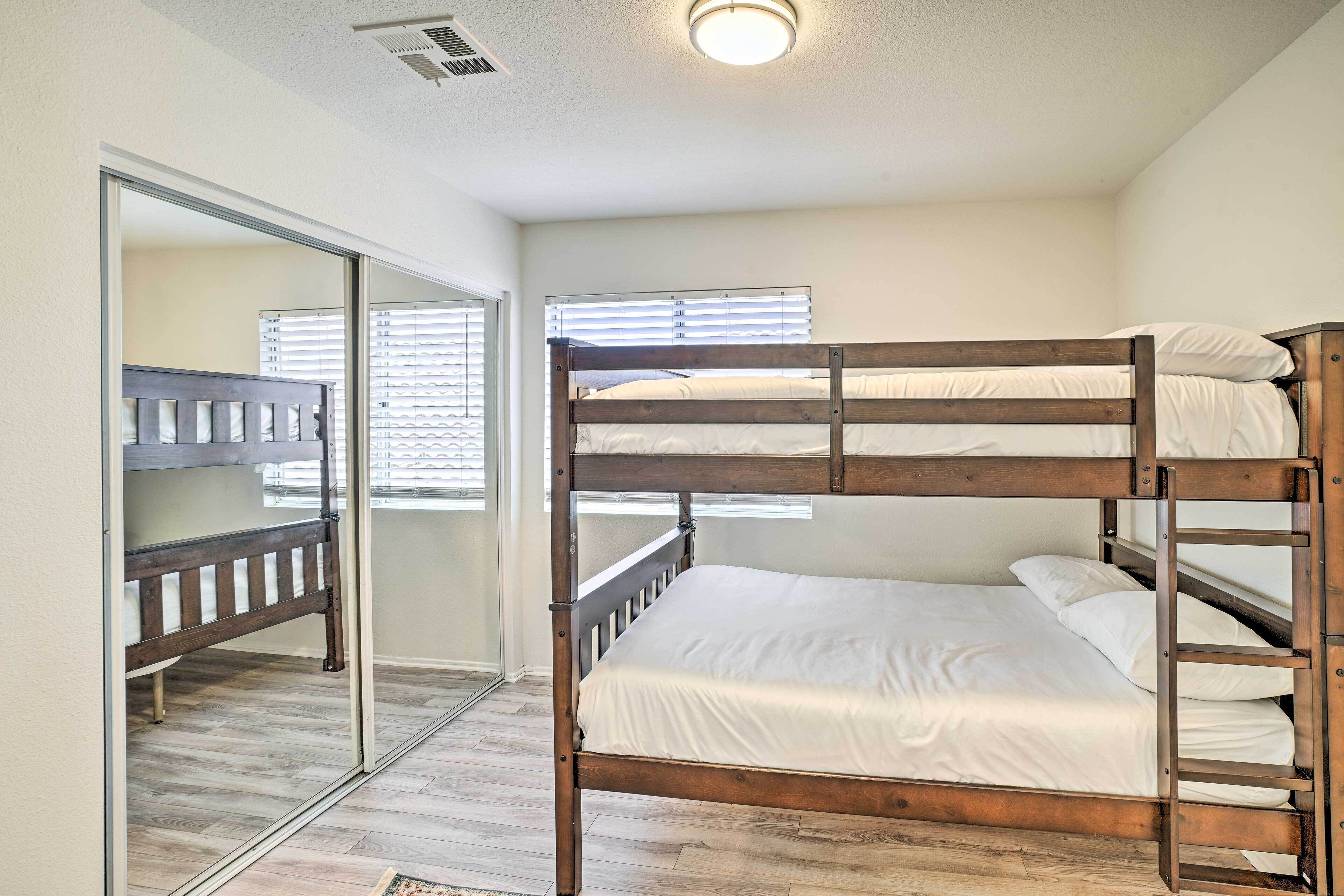 A bunk bed room with a wooden frame, white bedding, and a sliding door leading to another room.