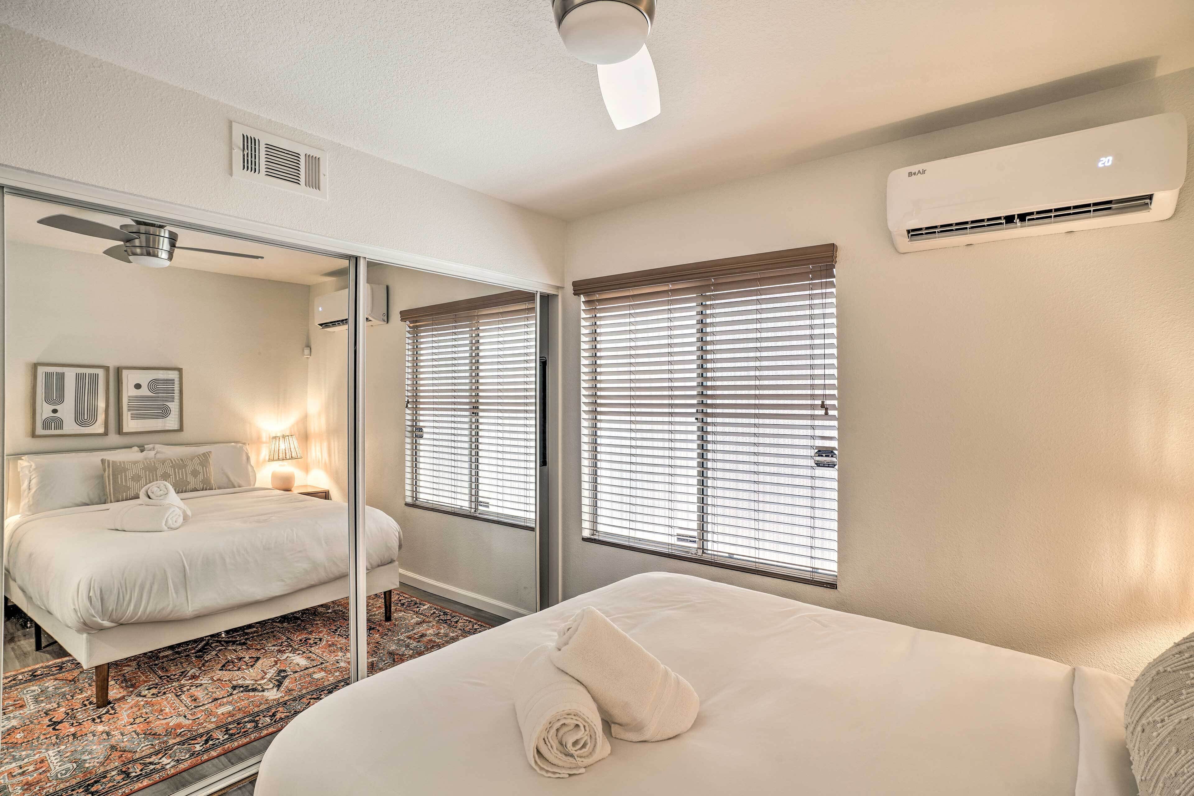 A modern hotel room with a large bed, a mirror, a ceiling fan, and an air conditioning unit.