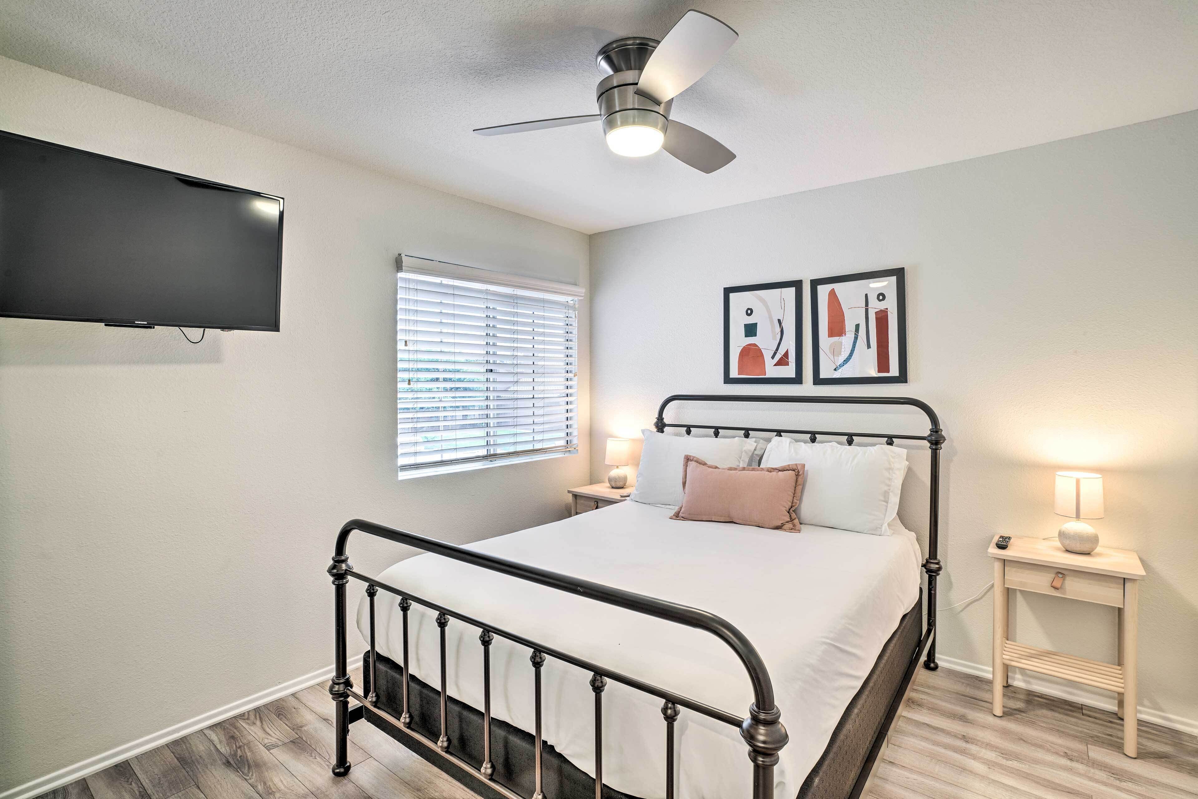 A bedroom with a bed, a ceiling fan, a TV mounted on the wall, and artwork on the wall.