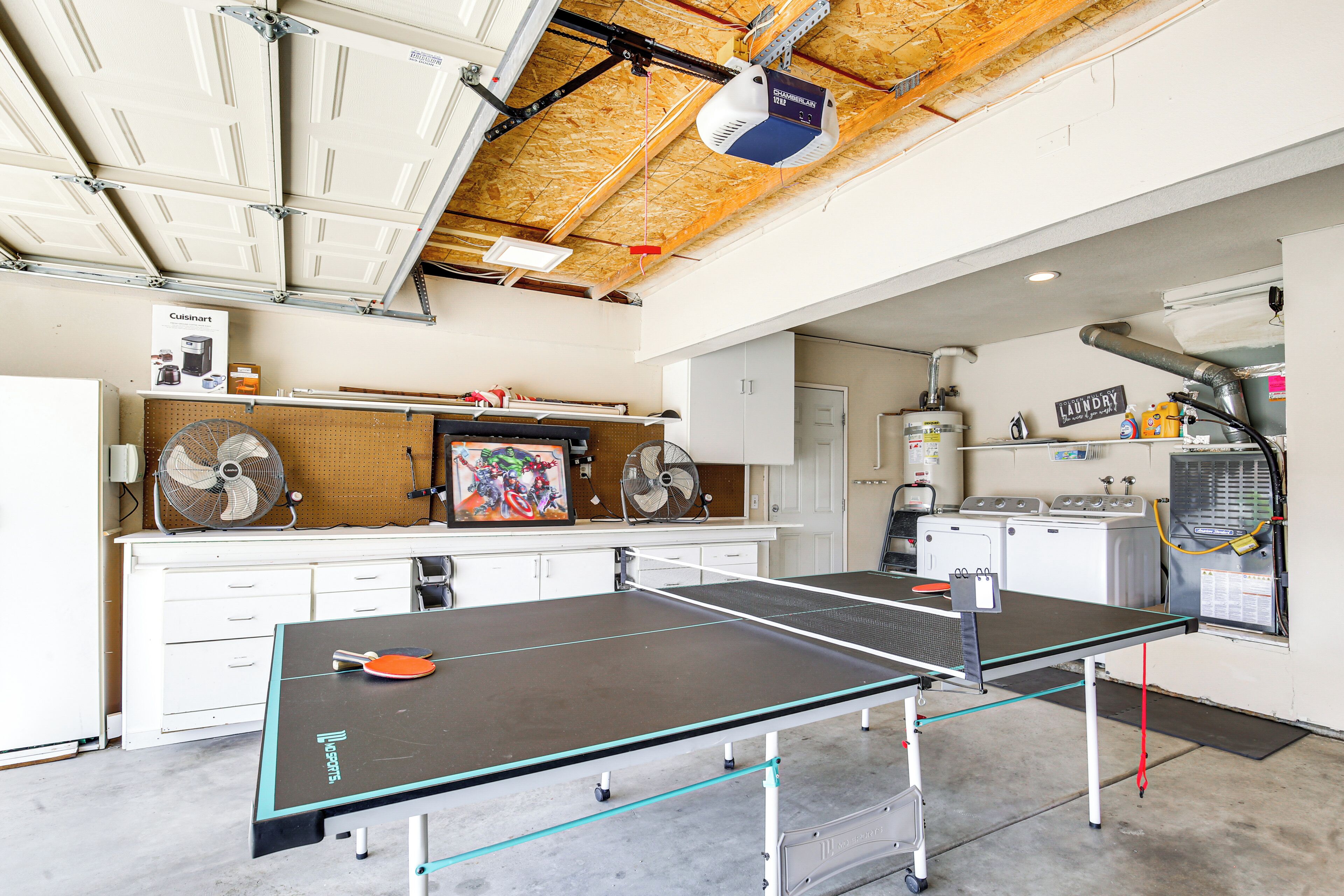 A ping pong table in a room with a ceiling fan, a painting, and a laundry area.