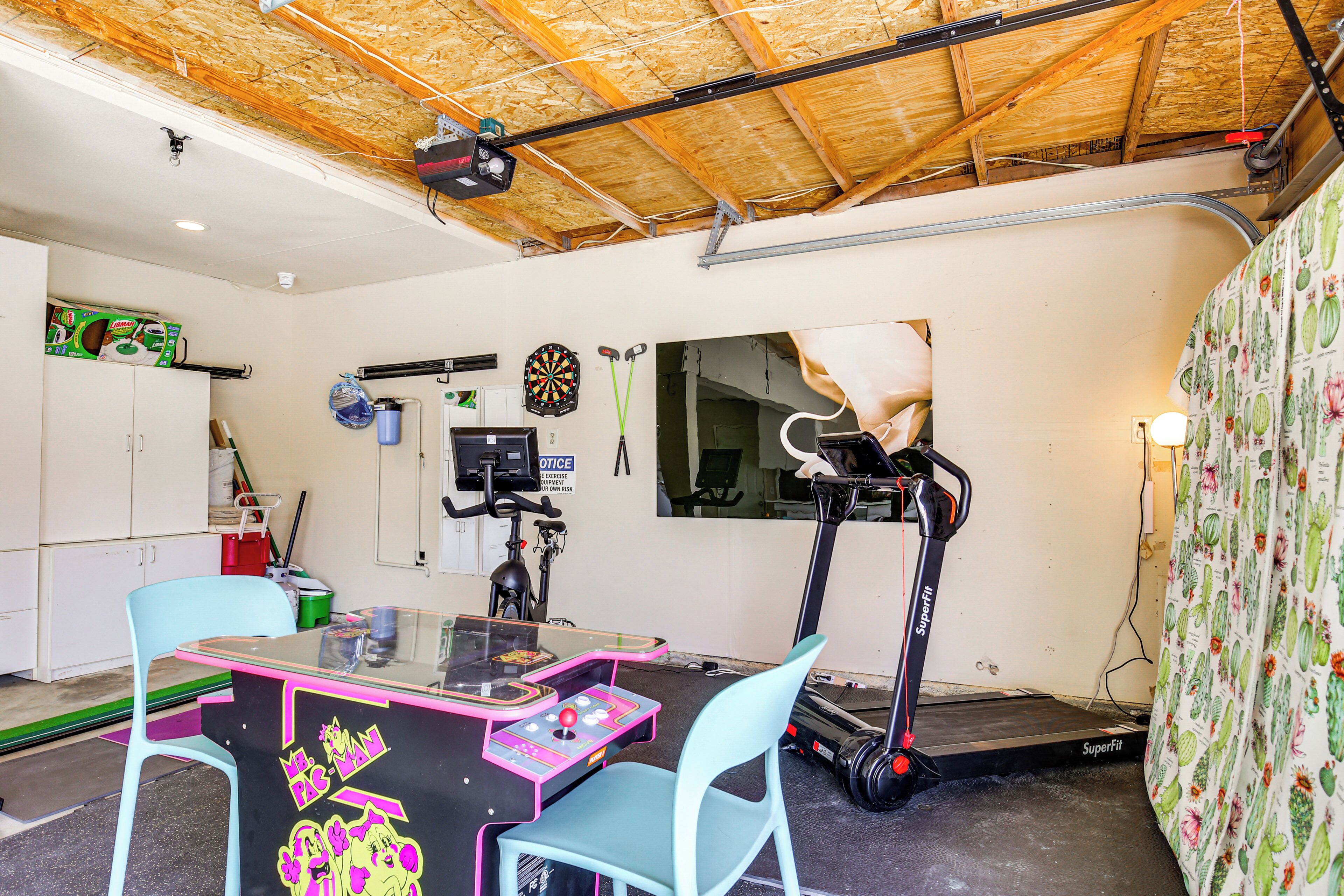 A room with a ping pong table, exercise equipment, and a dartboard.