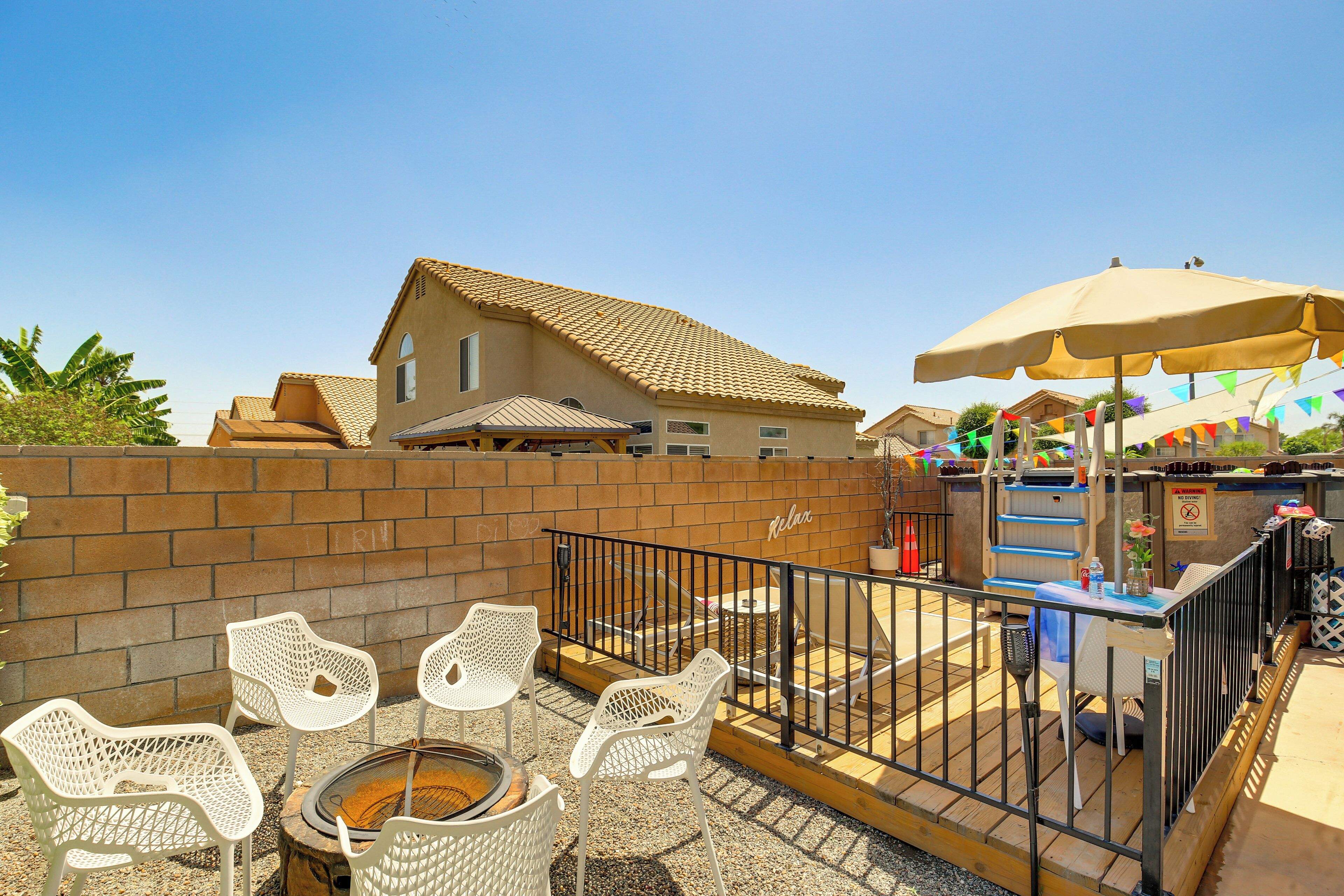 A patio area with white wicker chairs, a fire pit, and a wooden table.