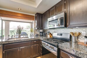 A modern kitchen with dark wood cabinets, stainless steel appliances, granite countertops, and a large window offering a view of the outdoors.