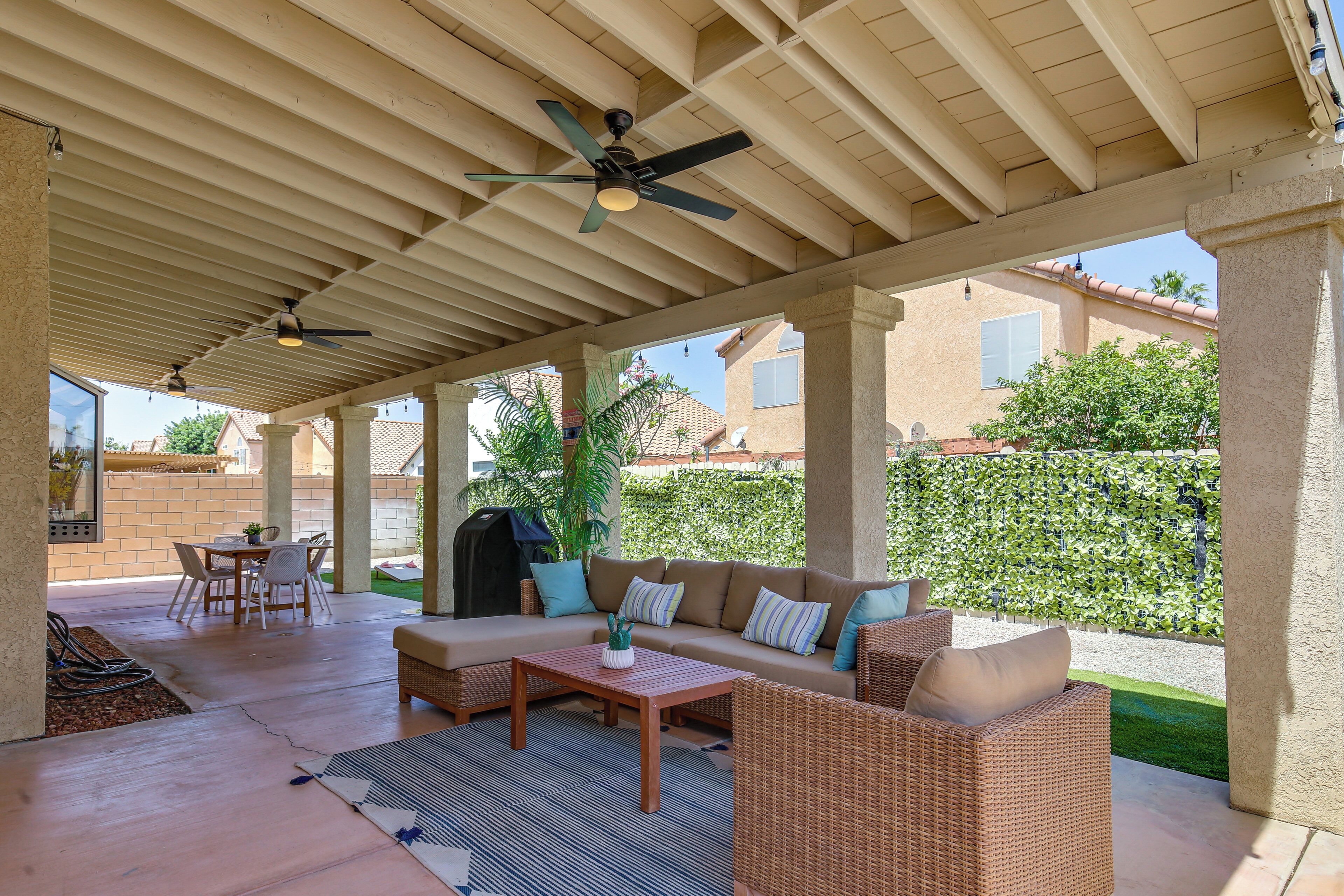 A covered patio area with a sofa, chairs, a table, and ceiling fans.