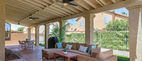 A covered patio area with a sofa, chairs, a table, and ceiling fans.