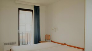 Una habitación de hotel con una cama, una silla, una ventana con cortinas y un radiador.