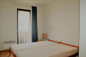 Una habitación de hotel con una cama, una silla, una ventana con cortinas y un radiador.