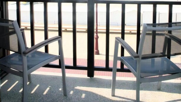 Un balcón con dos sillas y una mesa, con vista a una playa y un farol rojo.