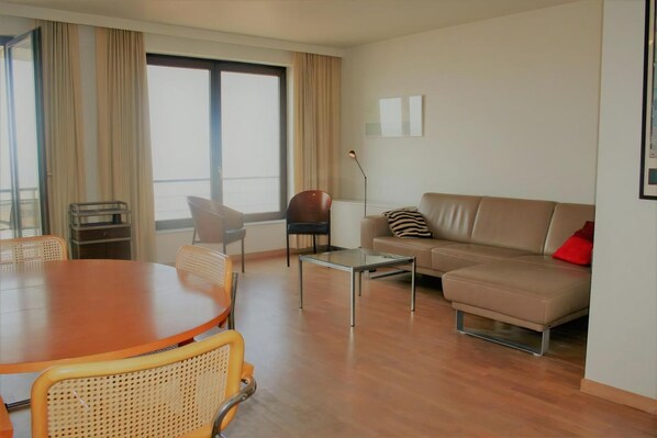 Una sala de estar moderna con una mesa de comedor de madera, dos sofás, una mesa auxiliar y un ventanal con cortinas.