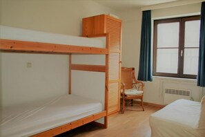 Habitación con literas, cabecera de madera, una silla, una ventana con cortinas y un radiador.