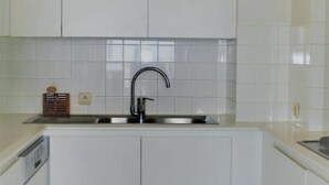 Una cocina con armarios blancos, un lavamanos de acero inoxidable y un salpicadero de azulejos.