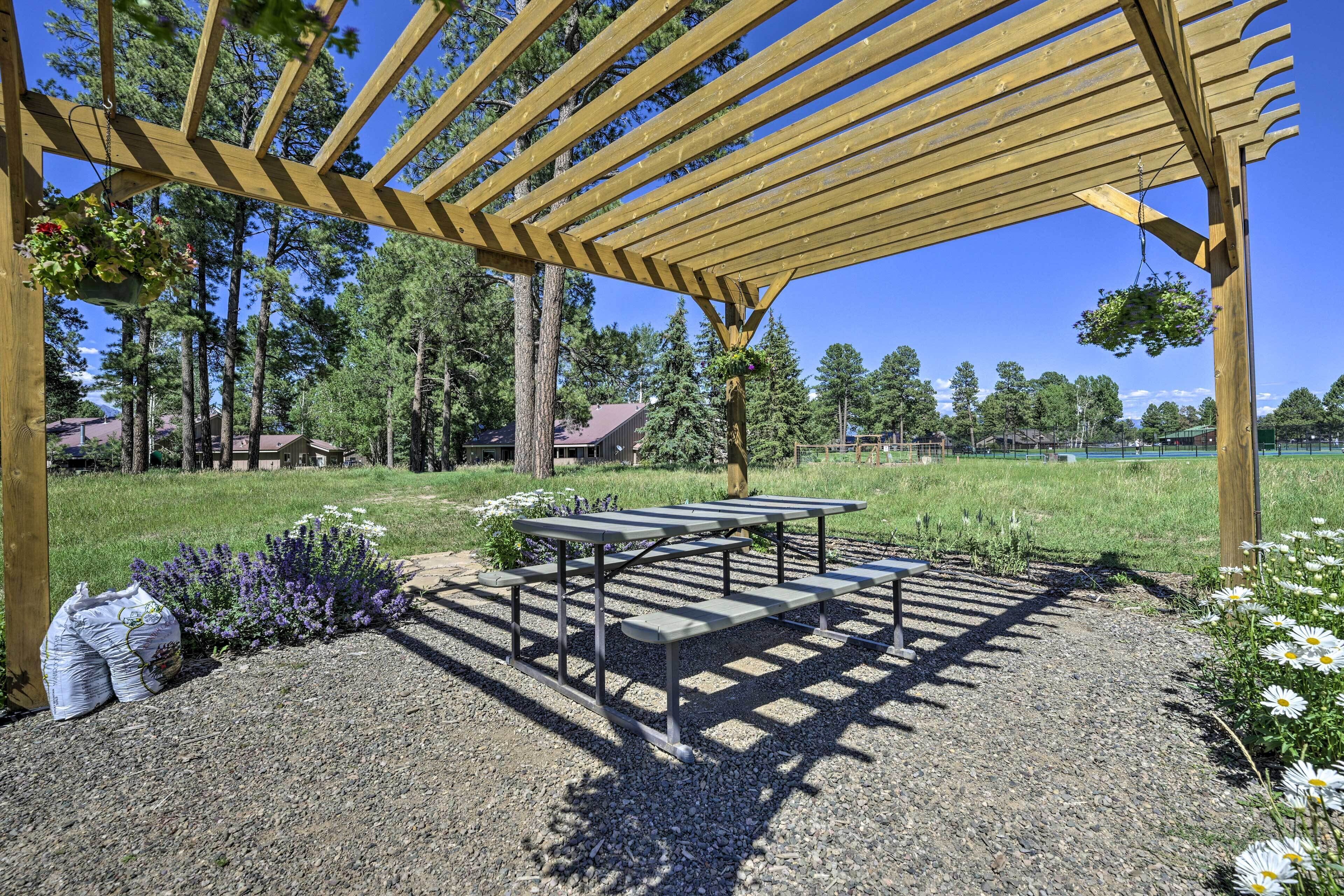 A wooden pergola with a gravel patio and picnic tables.