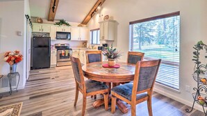 A modern kitchen with white cabinets, a central island, and a dining area with wooden chairs. - Cozy Pagosa Springs Townhome w/ Patio! (Pagosa Springs)