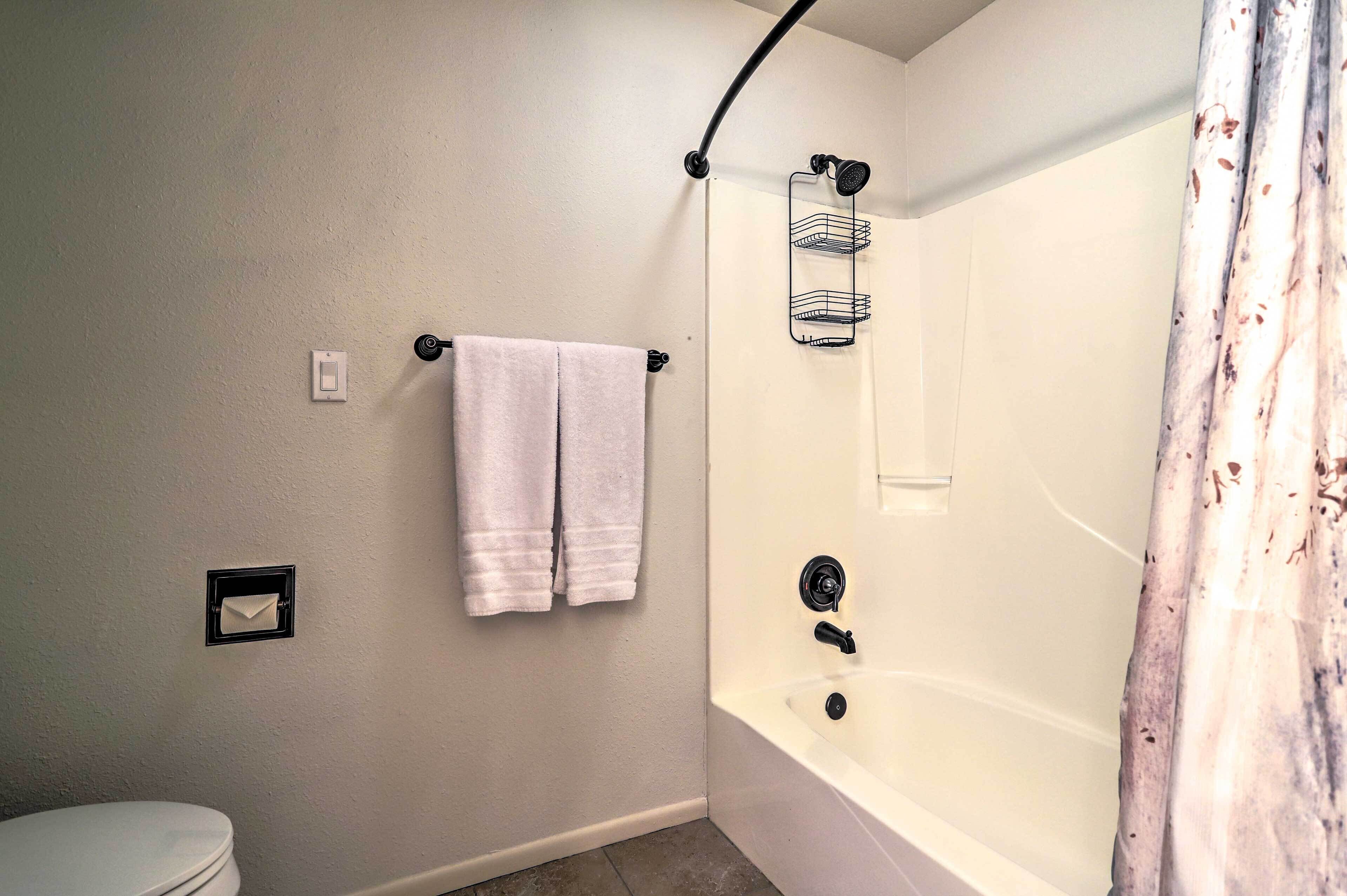 A bathroom with a toilet, a shower with a curved door, and a towel rack with two towels.