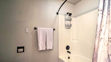 Un baño con inodoro, ducha con puerta curva y un perchero con dos toallas.