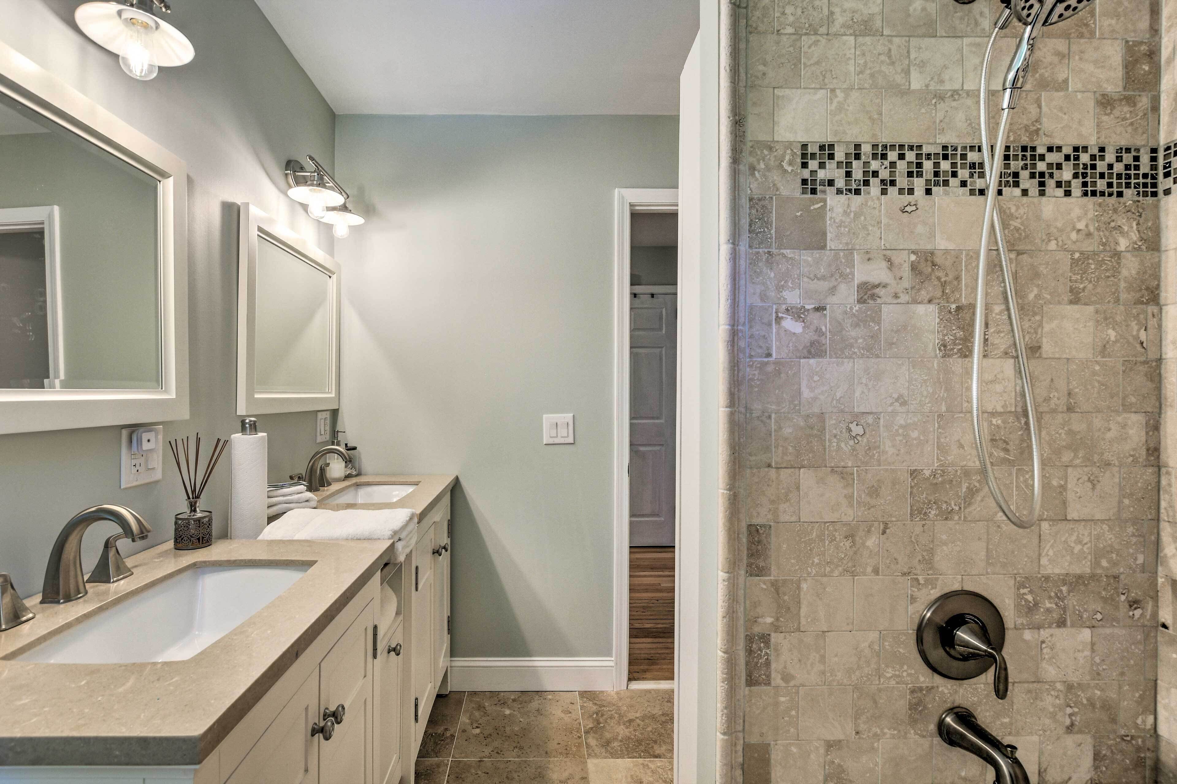 A bathroom with a double sink vanity, a shower with a tiled wall, and a door leading to a closet.