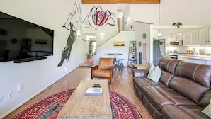A spacious living room with a brown leather sofa, a wooden coffee table, and a red patterned rug. A large wall mural depicts a heart and mountains. - Colorful Condo in Pagosa Springs w/ Patio! (Pagosa Springs)