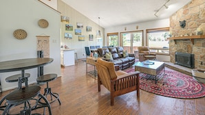 A spacious living room with a stone fireplace, wooden flooring, and a large window providing natural light. - Colorful Condo in Pagosa Springs w/ Patio! (Pagosa Springs)