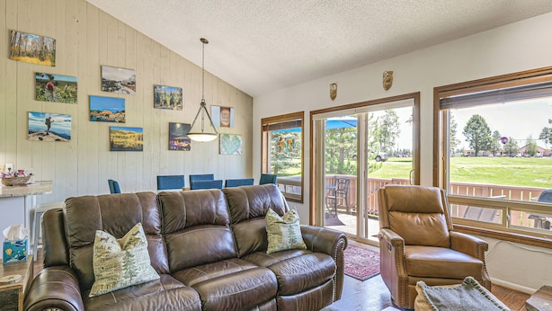 A living room with a brown leather sofa, a brown leather armchair, and a coffee table. There are several framed pictures on the wall and a window with a view of a green landscape. - Colorful Condo in Pagosa Springs w/ Patio! (Pagosa Springs)