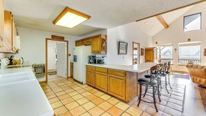 A spacious kitchen with wooden cabinets, a large island, and a dining area with bar stools. - New Mexico Cabin Hideaway w/ Eagle Nest Lake Views (Eagle Nest)