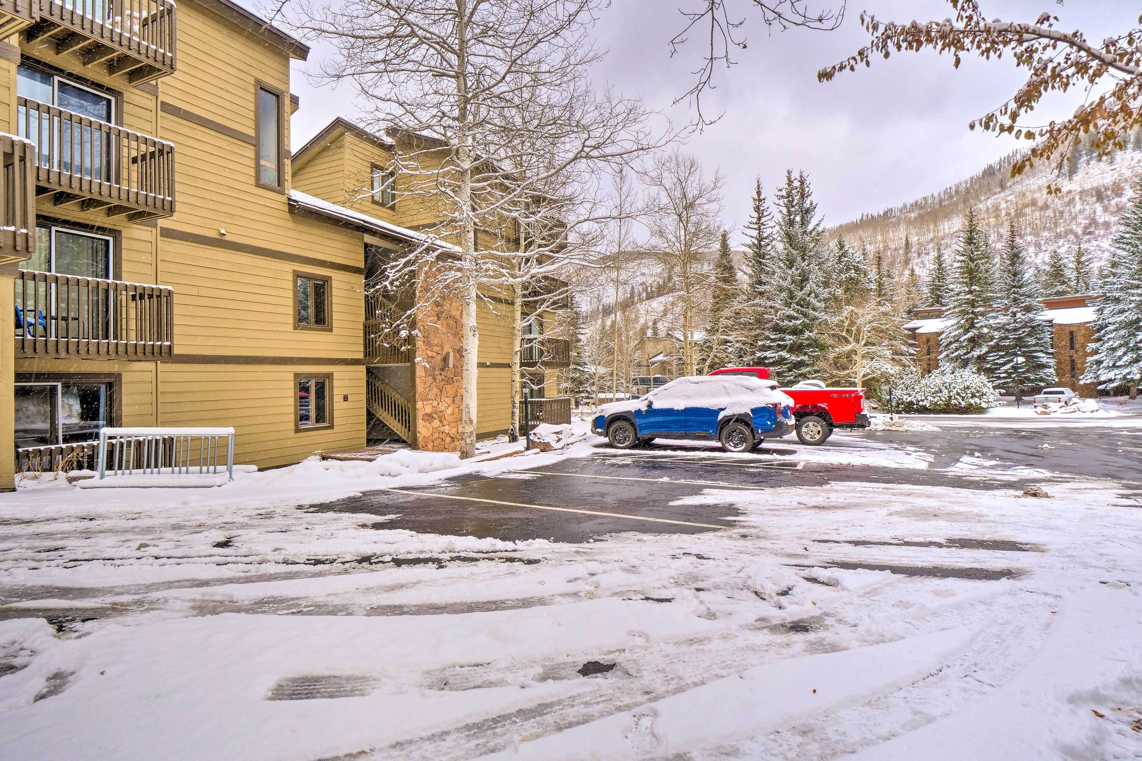 A multi-story building with balconies, a parking area with snow-covered ground, and a red vehicle parked in the lot.