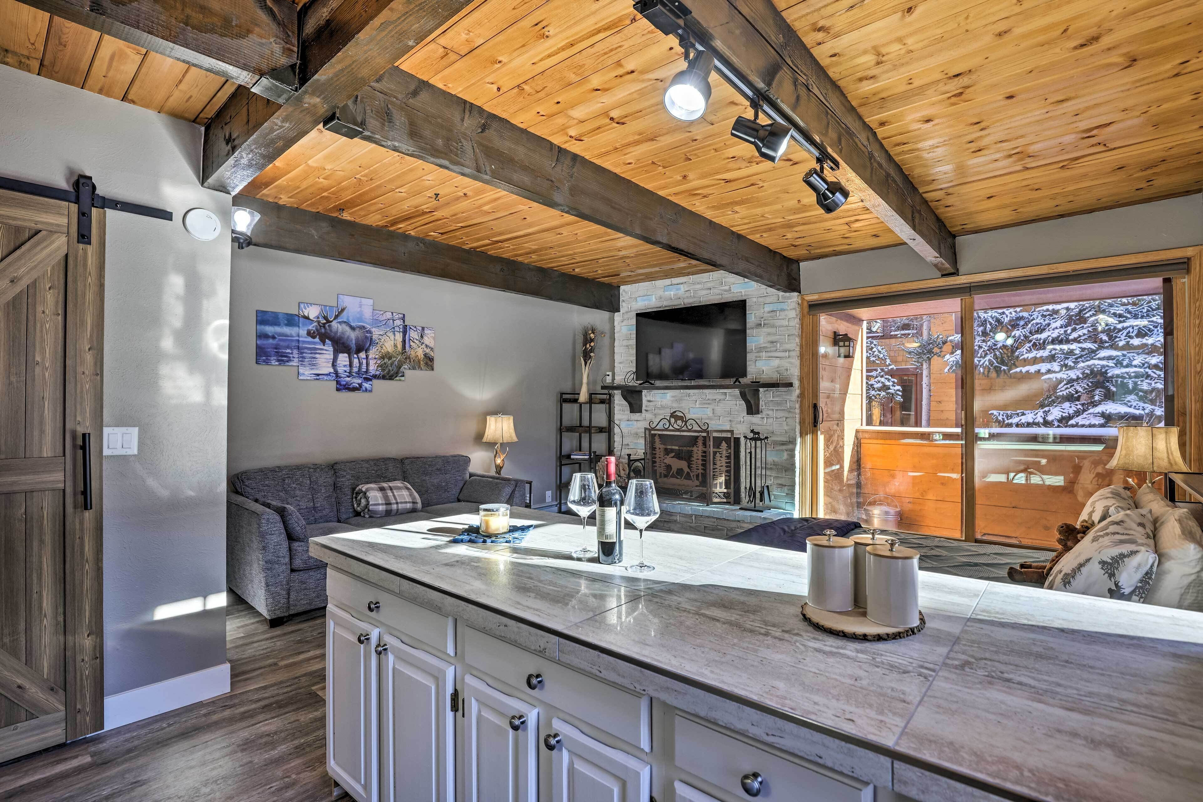 A cozy living area with a fireplace, a large window, and a wooden ceiling.