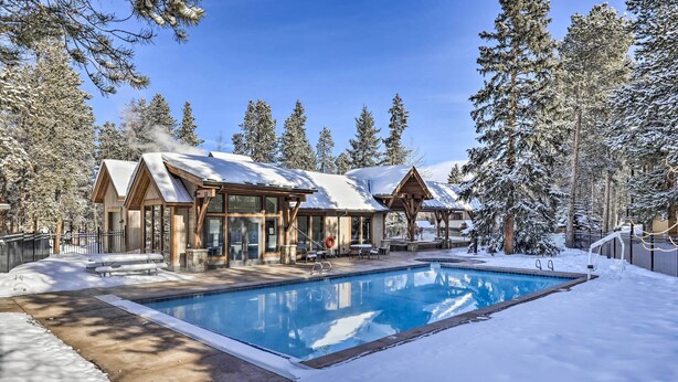 A resort with a swimming pool surrounded by snow-covered trees and a clear blue sky.