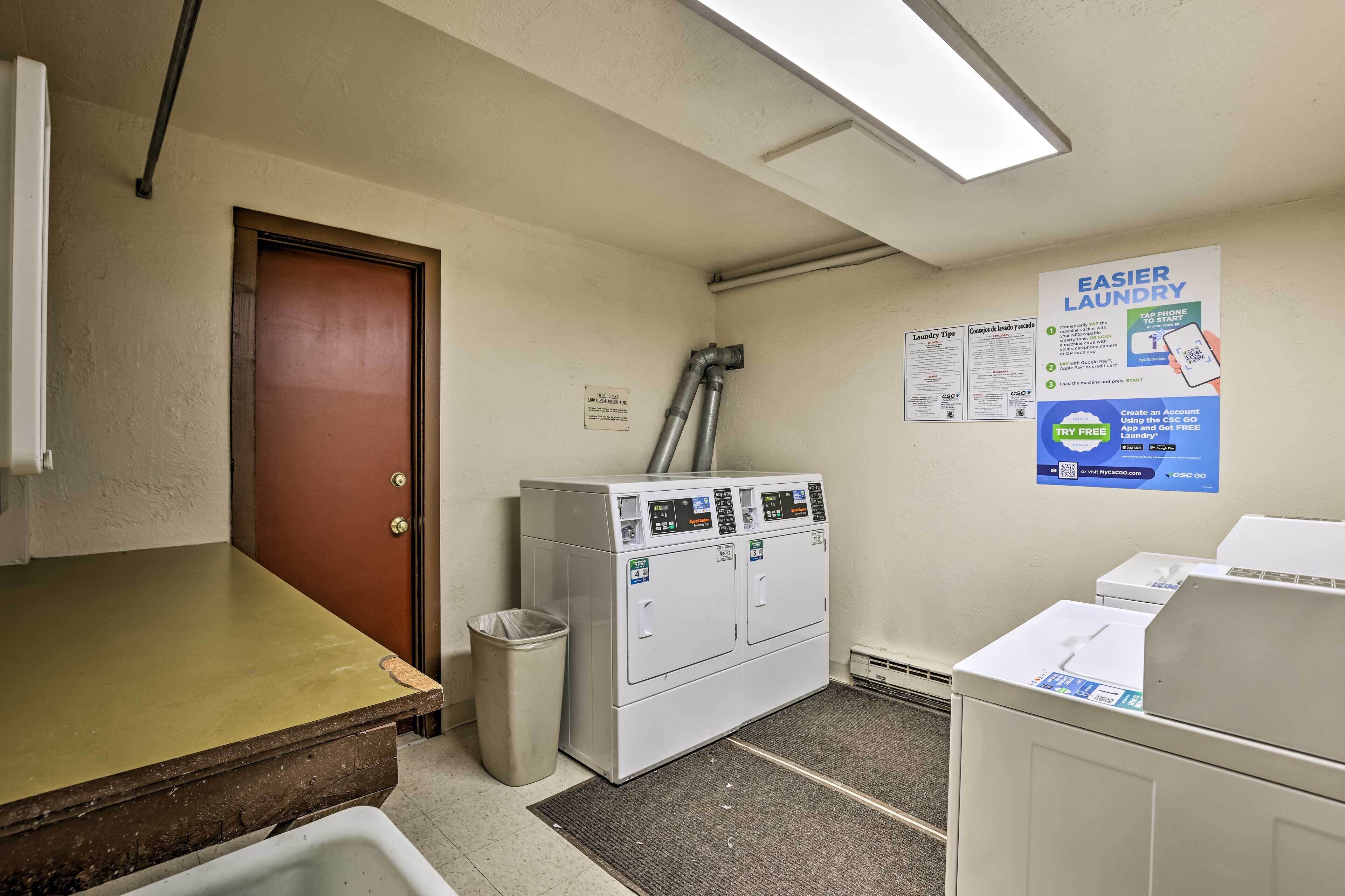 A laundry room with a washing machine, a dryer, a trash can, and a bulletin board with laundry tips.