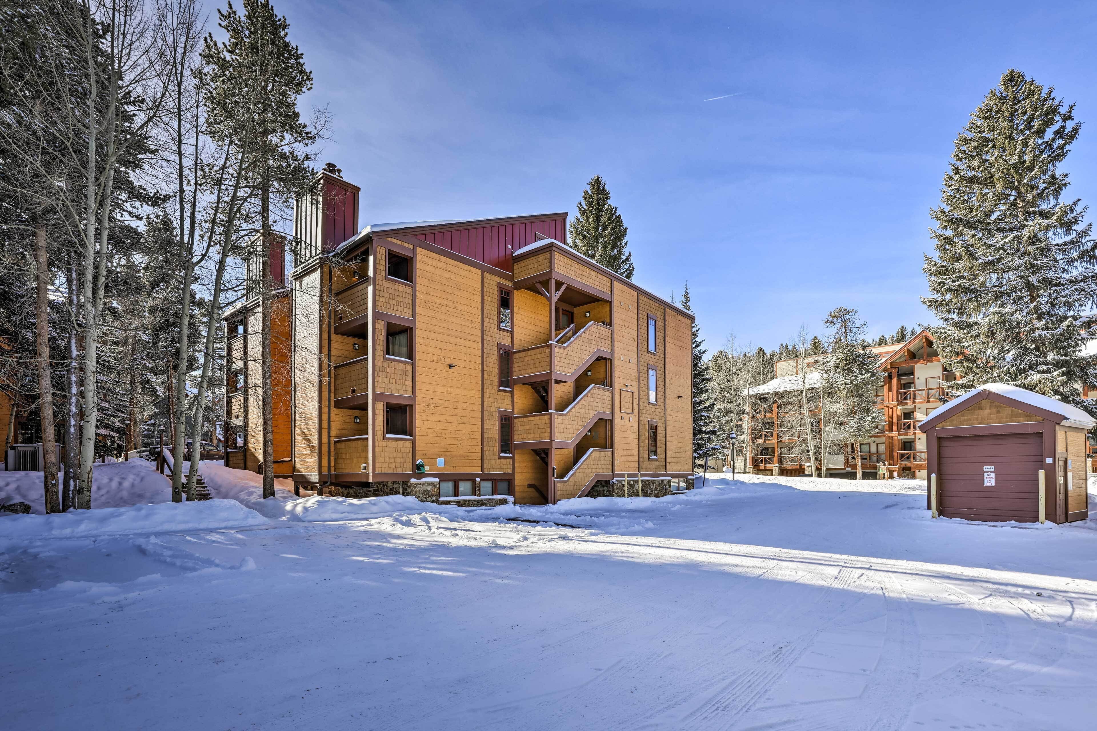Un edificio de madera de varios pisos con techo rojo, rodeado de árboles cubiertos de nieve y un cielo despejado.