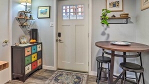 A small dining area with a round wooden table and two stools, a colorful bird-themed dresser, a lamp, and a door with a window. - 3 Mi to Dtwn: Convenient Denver Apt (Denver)