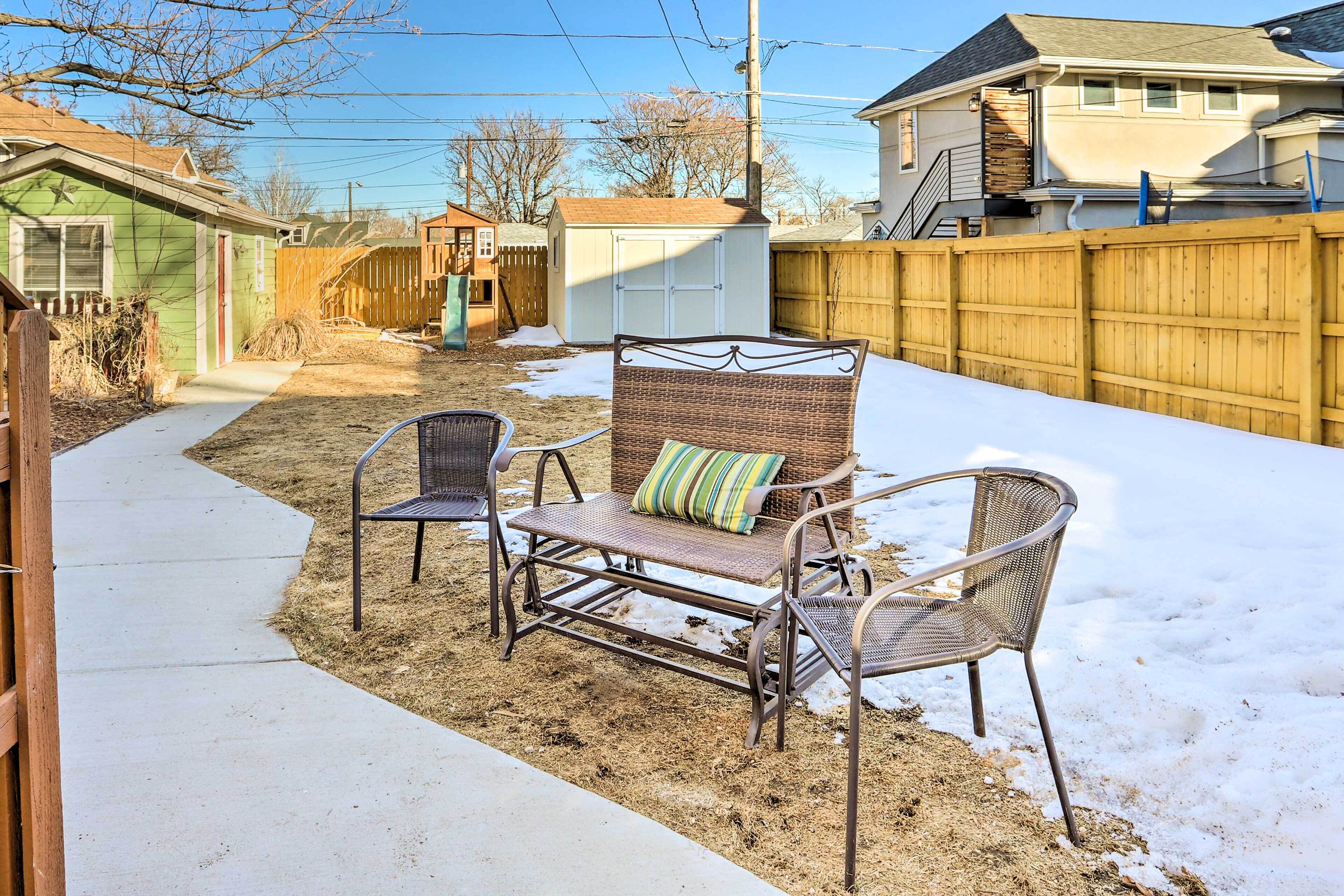 A backyard with a concrete pathway, a wicker table with chairs, and a small shed.