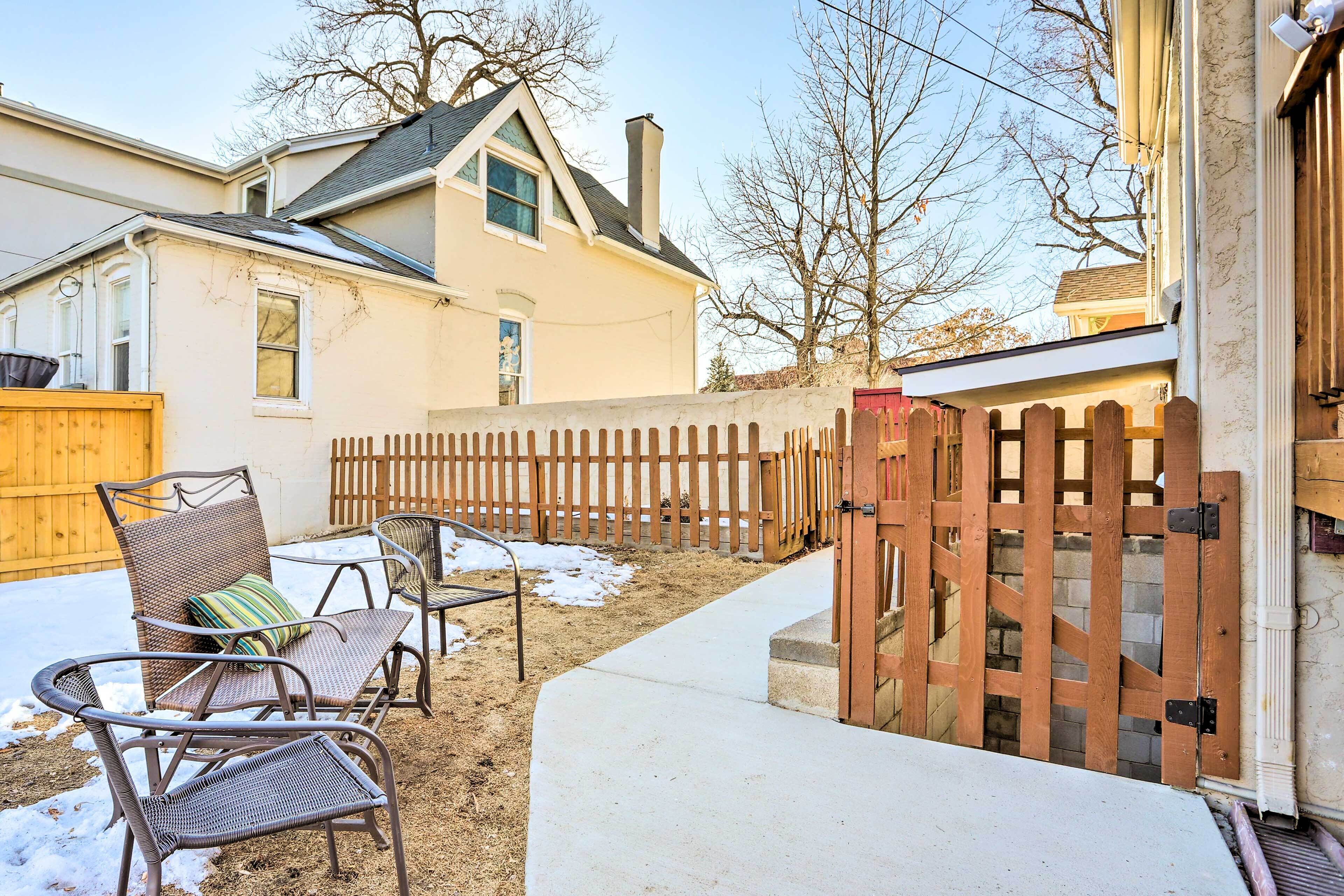 A backyard with a wooden fence, a concrete pathway, and outdoor furniture including a chair and a table.