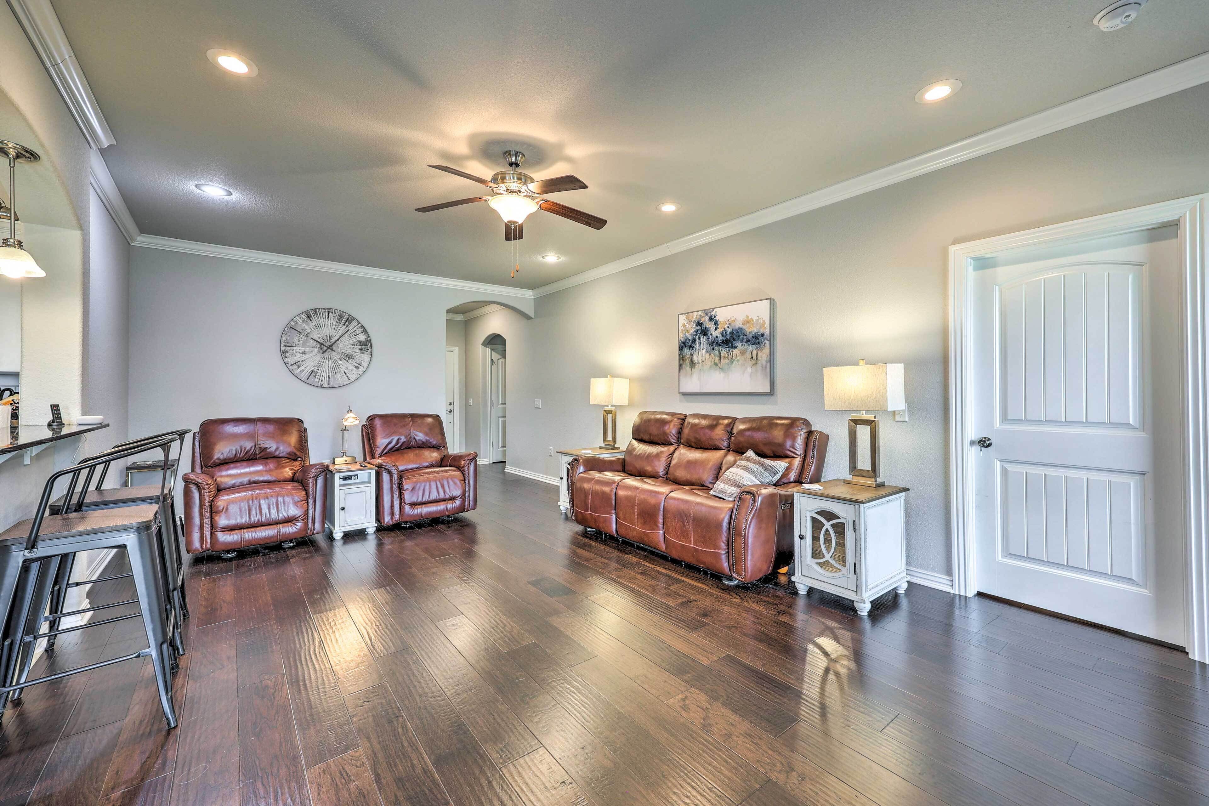 A living room with a ceiling fan, a clock, a sofa, two armchairs, a coffee table, and a door.
