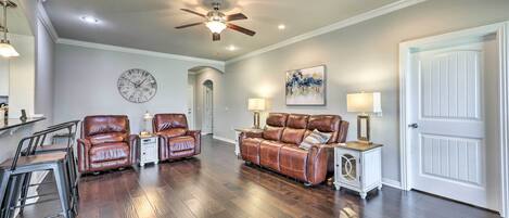 A living room with a ceiling fan, a clock, a sofa, two armchairs, a coffee table, and a door.