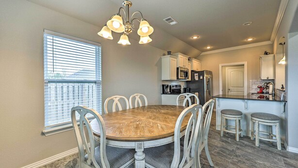 A dining area with a wooden table and white chairs, a kitchen with white cabinets and appliances, and a window with blinds. - Fayetteville Home: Near University & Biking Trails (Fayetteville)