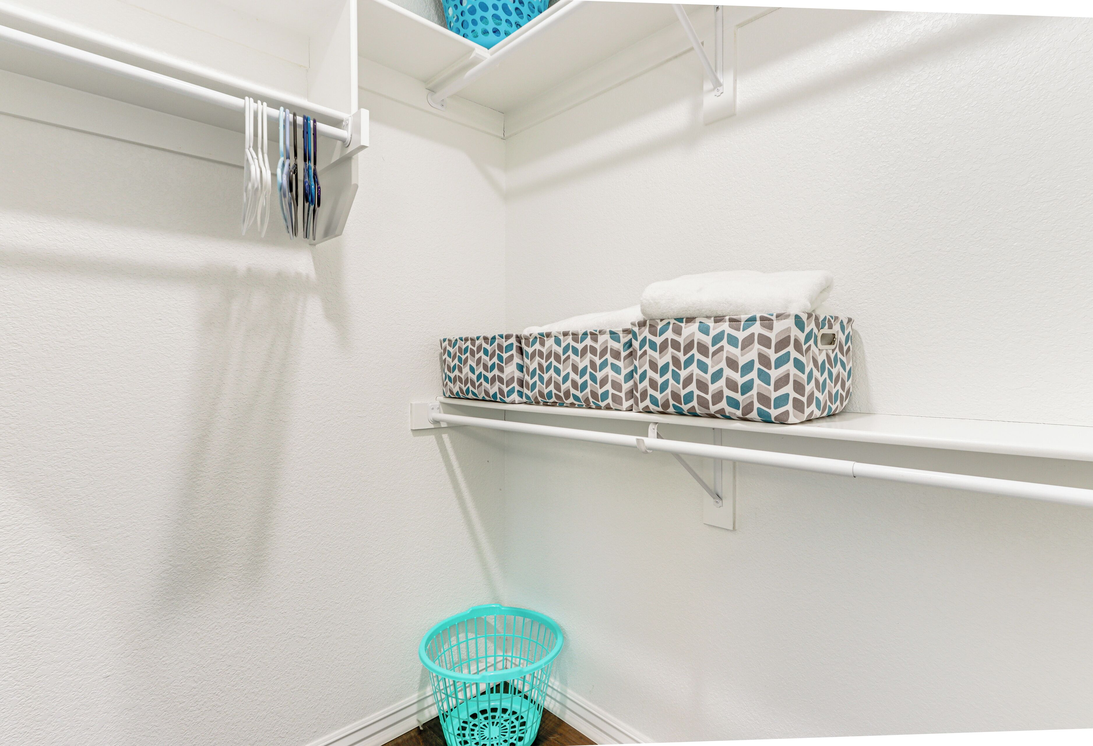 A laundry area with a white wall, a shelf with a patterned laundry basket, and a white towel on a shelf.