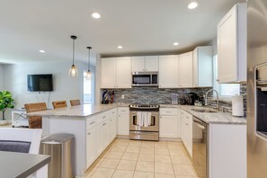 A modern kitchen with white cabinets, stainless steel appliances, a tiled backsplash, and pendant lighting.