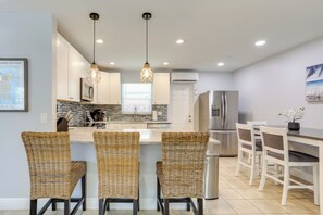 A modern kitchen with white cabinets, a central island with bar stools, stainless steel appliances, and pendant lighting.