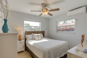 A bedroom with a bed, nightstand, dresser, ceiling fan, windows, and an air conditioning unit.