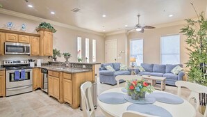 A modern kitchen with a built-in microwave, oven, and sink. There is a dining area with a white table and chairs, and a blue sofa in the living room. - South Padre Island Condo - 200 Ft to Beach! (South Padre Island)