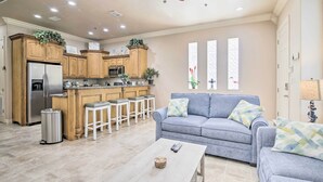 A modern kitchen with wooden cabinets, a stainless steel refrigerator, and a bar area with stools. - South Padre Island Condo - 200 Ft to Beach! (South Padre Island)